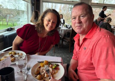 A man and woman smiling with a plate brimming with Christmas lunch in front of each other them. Turkey, potatoes and even Brussels sprouts.