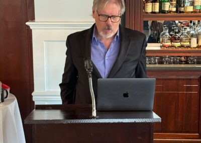 A man speaking at a podium to the many guests in the room, looking down at his computer.