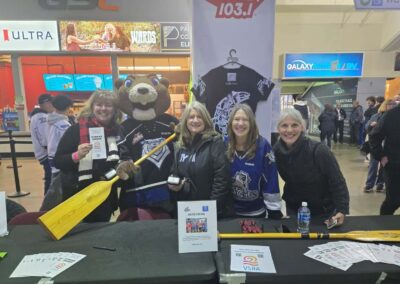 four women and the Victoria Royals mascot in front of a table holding VSRA info and a paddle
