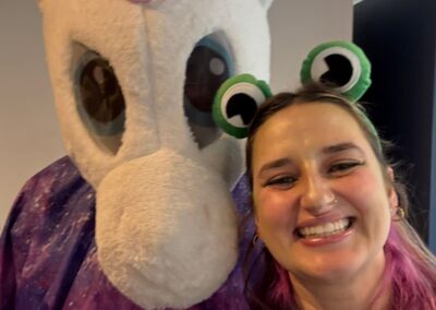 A person in a unicorn costume and a smiling woman with a frog ear headband and pink hair.