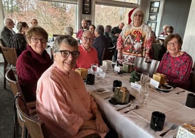 A room full of happy people sitting at dining tables. One room standing up with a Santa hat and crazy Christmas sweater.