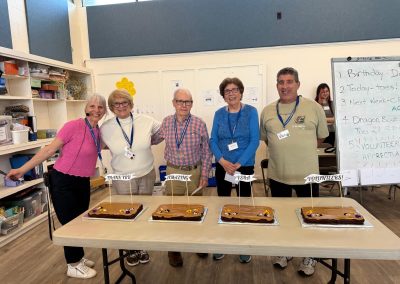 A group of men and women standing in front of a table with four cakes on it.