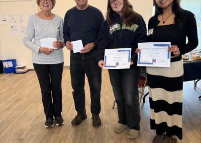 Two young women, one older woman and an older man standing holding certificates smiling