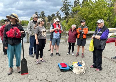 Group of people in life preservers, one person holding a paddle, on a dock with dragon boats.