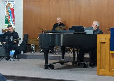 Three men playing guitar, drums and piano