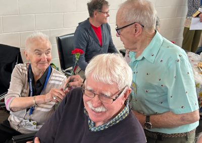 An elderly man giving a carnation to an elderly, smiling woman.