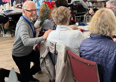 Smiling elderly man kneeling by a woman at a table, with a bunch of carnations.