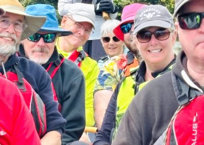 A group of smiling adults sitting in a boat holding paddles.