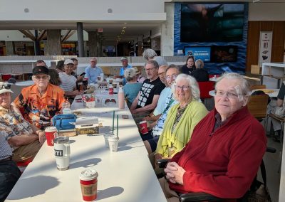 Men and women sitting at a long table with coffee cups in front of them at Hillside Mall's food court.