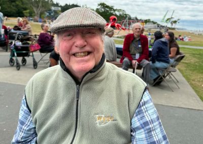 An elderly man wearing a British flat cap smiling.