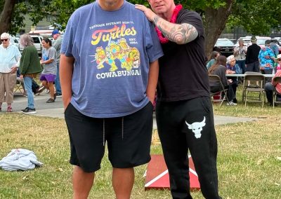 Two men standing together. One man is wearing a Turtles "Cowabunga" t-shirt.