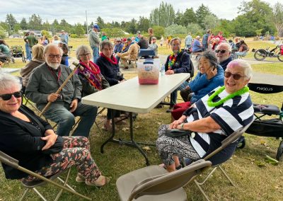 Eight smiling older people sitting around a picnic table, some of them wearing colourful leis. No food yet, but they look happy.