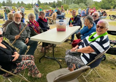 Eight smiling older people sitting around a picnic table, some of them wearing colourful leis. No food yet, but they look happy.
